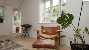 A modern room with a wooden floor, a leather chair with a cushioned seat, a black potted plant, and a window with a view of greenery. - 4 Star Holiday Home in Ebeltoft (Ebeltoft)