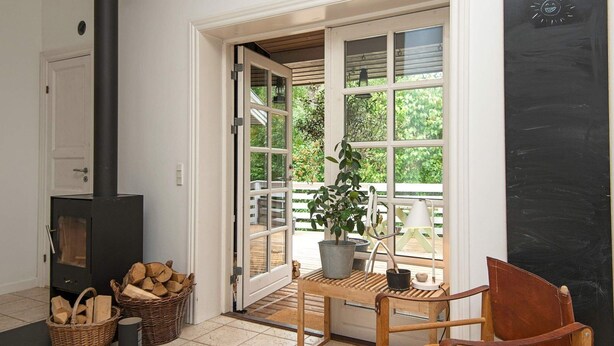 A cozy living room with a fireplace, a wooden chair, a potted plant, and a large window. - 4 Star Holiday Home in Ebeltoft (Ebeltoft)