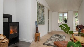 A living room with a fireplace, wooden flooring, a large plant, and a view of the outdoors. - 4 Star Holiday Home in Ebeltoft (Ebeltoft)