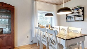 Un espace repas avec une table en bois et des chaises blanches, un buffet en bois et des luminaires suspendus.