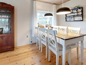 Een eetgedeelte met een houten tafel, witte stoelen, een houten kast en hanglampen.