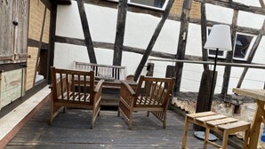 Une terrasse en bois avec une table et des chaises, une lampe et une vue sur un bâtiment blanc aux poutres apparentes.