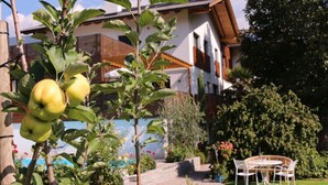 Un jardín residencial con una mesa y sillas en el patio, un árbol frutal y una casa con techo de tejas.