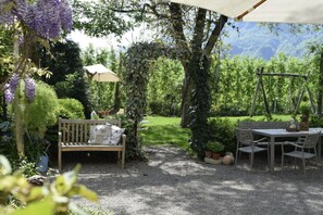 A garden patio with a wooden bench, a table with chairs, and a swing set. - Holiday Apartment Krosshof (Nalles)