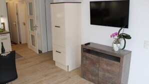 Ett modernt vardagsrum med en platt-TV som hänger på väggen, ett träskåp med en vas med blommor och en svart stol.