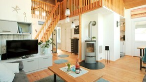 Uma sala de estar ampla com escada de madeira, TV, mesa de jantar e lareira.