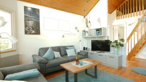 Uma sala de estar moderna com um sofá cinzento, mesa de centro de madeira e televisão de tela plana.