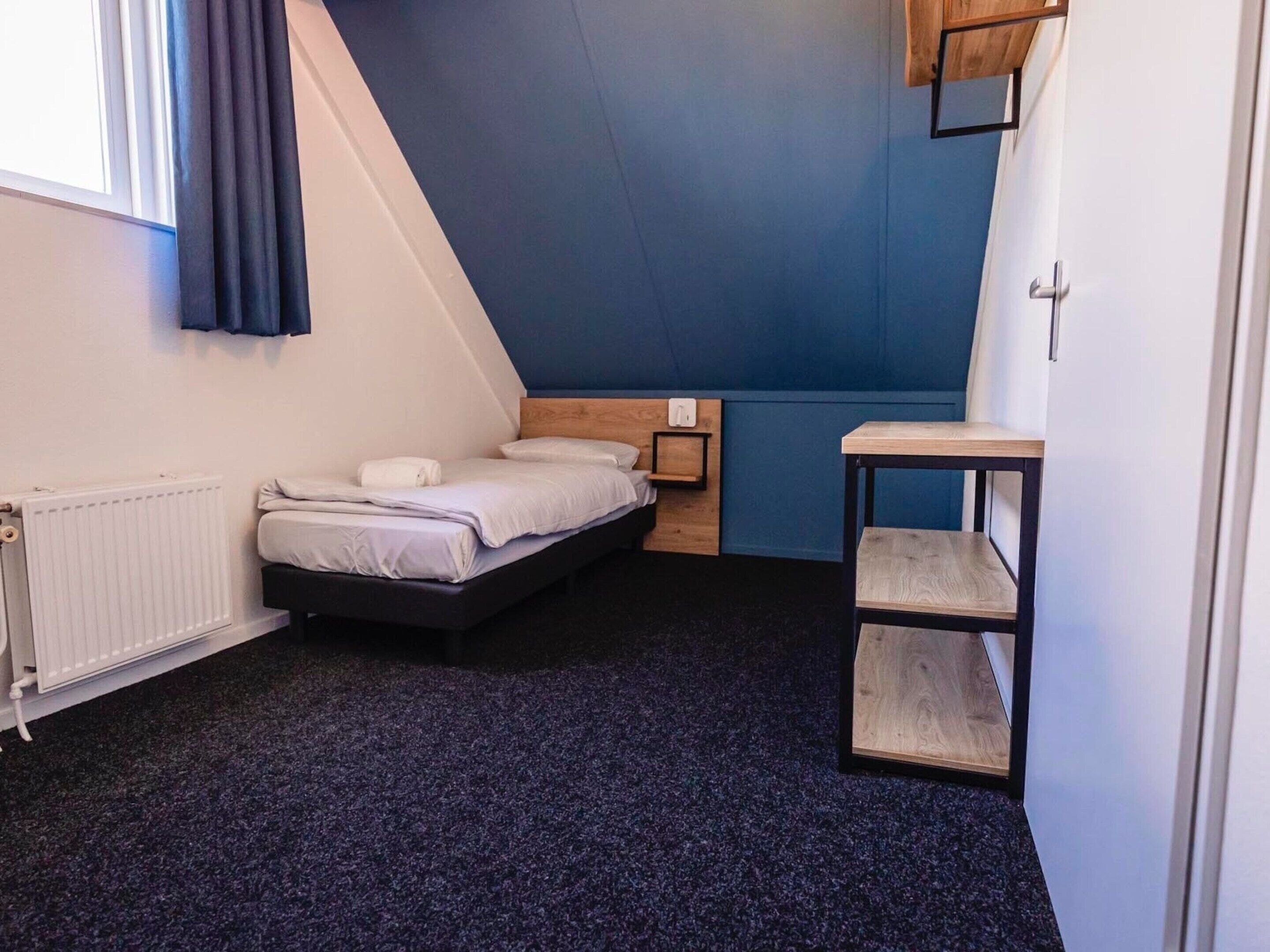 A small, modern bedroom with a bed, a wooden nightstand, a small table, and a radiator.