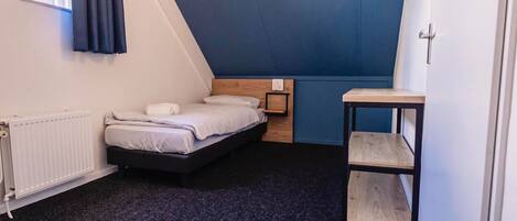 A small, modern bedroom with a bed, a wooden nightstand, a small table, and a radiator.