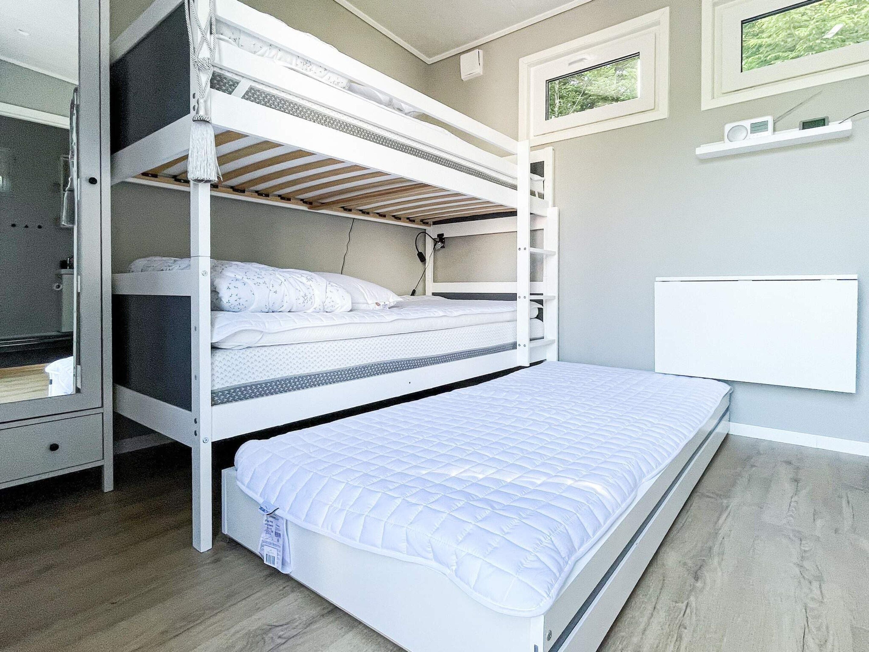 A bunk bed room with a white mattress, a lower bunk with a mattress, and a white headboard.
