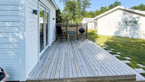 A deck with a grill and chairs, a covered patio area, and a house with a white exterior. - 3 Person Holiday Home in Ljungby (Ljungby)