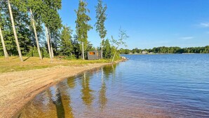 A lakeside view with a clear water body, a grassy area, and a small structure by the water's edge. - 3 Person Holiday Home in Ljungby (Ljungby)