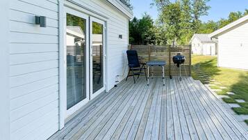 A deck with a table and chairs, a grill, and a sliding glass door leading to a covered patio.