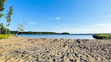 Una playa arenosa con vista despejada a un lago y una isla boscosa en la distancia.