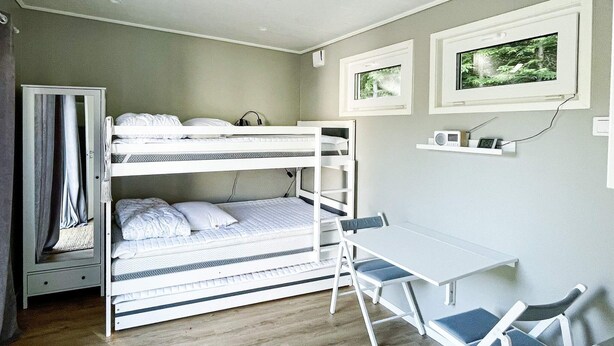 A bunk bed with a desk and chairs, a small shelf with items, and a window with a view of trees. - 3 Person Holiday Home in Ljungby (Ljungby)