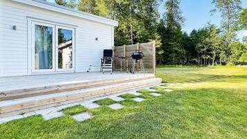 A modern white building with a deck, a grill, and a chair.