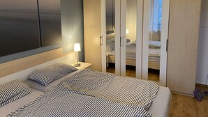 Et soveværelse med seng, natborde, lampe og et garderobeskab med spejle.