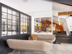 Een modern interieur met een bank, een groot raam en een bord waarop 'BOWLING' staat.