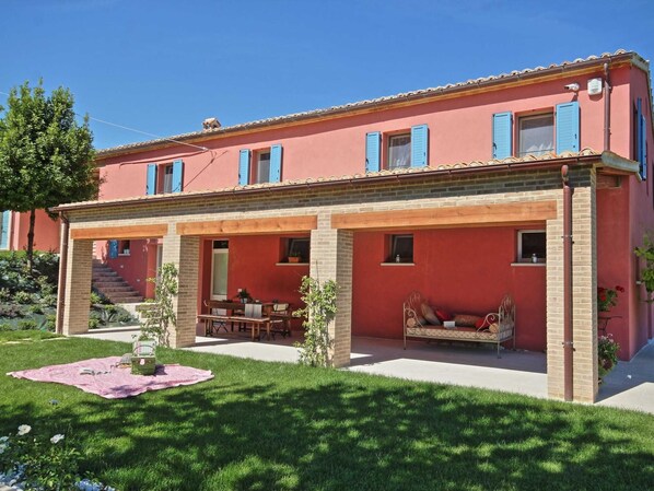 Una casa de dos pisos con fachada roja, contraventanas azules y un porche cubierto con mobiliario exterior.