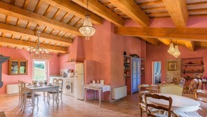 Una cocina amplia con vigas de madera, un comedor con mesa y sillas, y una sala de estar con un sofá y un sillón estampado.