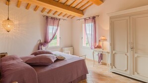 Un dormitorio con cama, un armario, una mesa con lámpara y una ventana con cortinas.