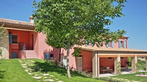 Una villa rosa con un sendero de piedra que lleva a la entrada, un porche cubierto y un césped verde y exuberante.