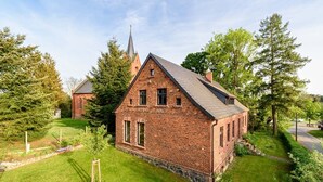A small brick building with a steeply pitched roof, surrounded by a well-maintained lawn and trees.