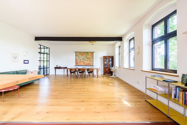 Una habitación amplia con suelo de madera, una mesa de comedor con sillas, un sofá y una estantería.