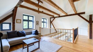 A spacious loft with exposed wooden beams, a sofa, a coffee table, and a staircase leading to an upper level.