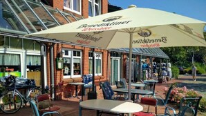 An outdoor seating area with tables and chairs, a bicycle parked nearby, and a large umbrella providing shade. - Sun, Mudflats and sea (Wurster Nordseeküste)