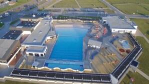 An aerial view of a swimming pool complex with multiple pools, a parking area, and surrounding fields. - Sun, Mudflats and sea (Wurster Nordseeküste)