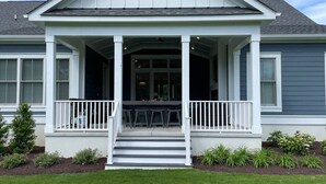 Ein Haus mit überdachter Veranda, Treppen zum Eingang und einem kleinen Garten.