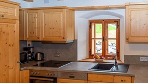 A kitchen with wooden cabinets, a stove, oven, and a window with a view of greenery. - Infanglalm "traunsee" (Altmuenster)