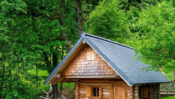 A rustic log cabin with a wooden porch and picnic table, surrounded by lush greenery. - Infanglalm "traunsee" (Altmuenster)
