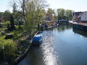 A canal with a covered boat docked on the right, surrounded by greenery and buildings.