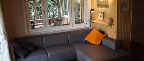 A modern living room with a grey sectional sofa, a small ottoman, and a wooden wall with a clock and picture frames.