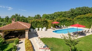 A backyard with a swimming pool, lounge chairs, and a covered patio area. - Villa Regenboog (Porec)