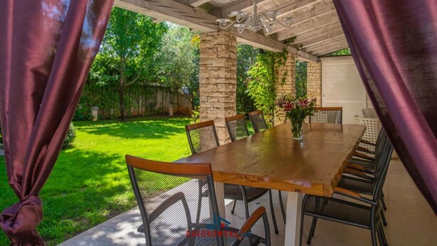 An outdoor patio with a wooden table and chairs, stone pillars, and a view of a lush garden. - Villa Regenboog (Porec)