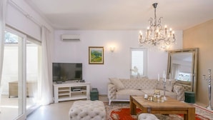 A living room with a television, sofa, ottoman, and chandelier. - Villa Regenboog (Porec)