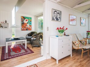 Ett rymligt vardagsrum med trägolv, en vit soffa, ett matbord med stolar, ett vitt skåp och en färgstark, abstrakt tavla.