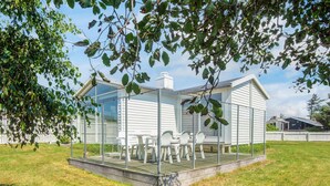 A glass-enclosed patio with a table and chairs, surrounded by a white fence and a tree. - 4 Person Holiday Home in Blokhus (Blokhus)