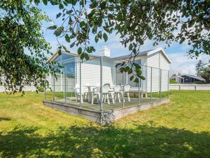 A glass-enclosed patio with a table and chairs, surrounded by a white fence and a tree. - 4 Person Holiday Home in Blokhus (Blokhus)