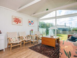 A spacious living room with a large window, wooden furniture, and a view of the garden. - 4 Person Holiday Home in Blokhus (Blokhus)