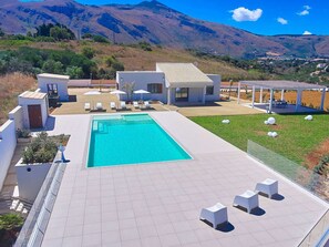 A modern pool area with a rectangular pool, lounge chairs, and a covered seating area. - Belvilla by OYO Villa Etesiae (Castellammare del Golfo)
