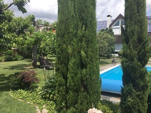 Un patio trasero residencial con piscina, altos árboles de hoja perenne, césped y una silla.