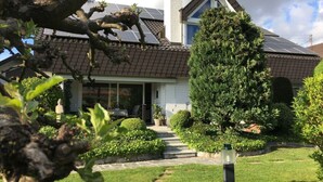 A house with a sloped roof, solar panels, a well-maintained lawn, and a large evergreen tree. - Holiday Apartment Helde Hochberg (Sasbach am Kaiserstuhl)