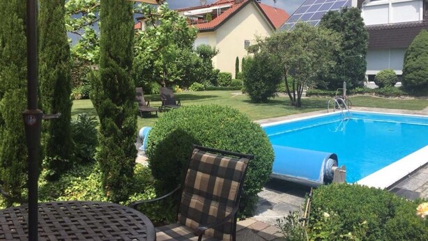 A backyard with a swimming pool, patio furniture, and a large umbrella. - Holiday Apartment Helde Hochberg (Sasbach am Kaiserstuhl)
