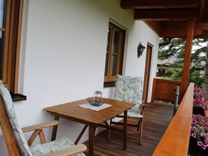 A wooden deck with a table and chairs, a small table with a candle, and a flower planter. - Kehlstein - Reich Family (Schoenau am Koenigssee)