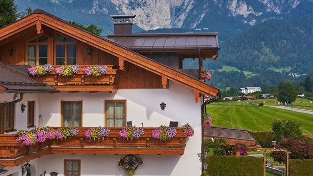 A traditional chalet with wooden balconies adorned with flower boxes, set against a backdrop of mountains. - Kehlstein - Reich Family (Schoenau am Koenigssee)
