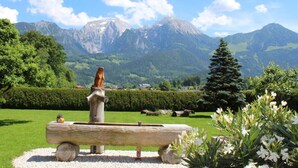 A wooden bench with a sculpture in a garden with mountains in the background. - Kehlstein - Reich Family (Schoenau am Koenigssee)